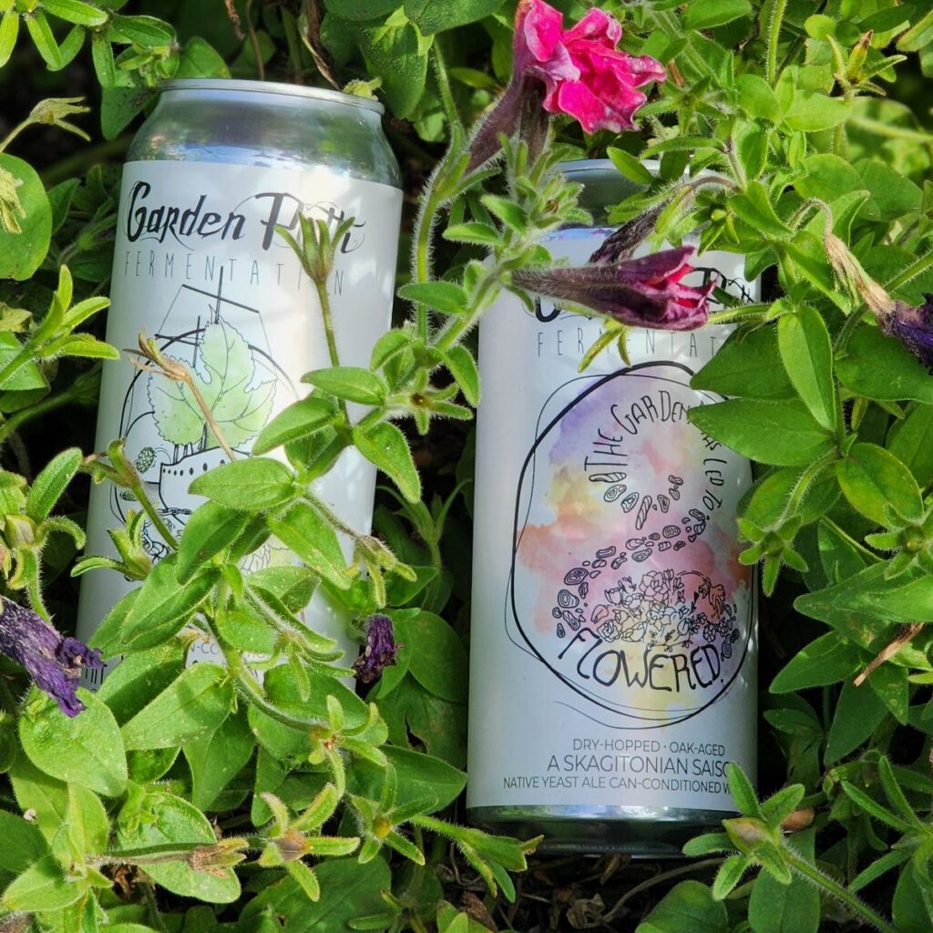 A can of The Garden Paths Led to Flowered and a can of The Wet Hopped Ship from Garden Path Fermenation semi-hidden in a plant.